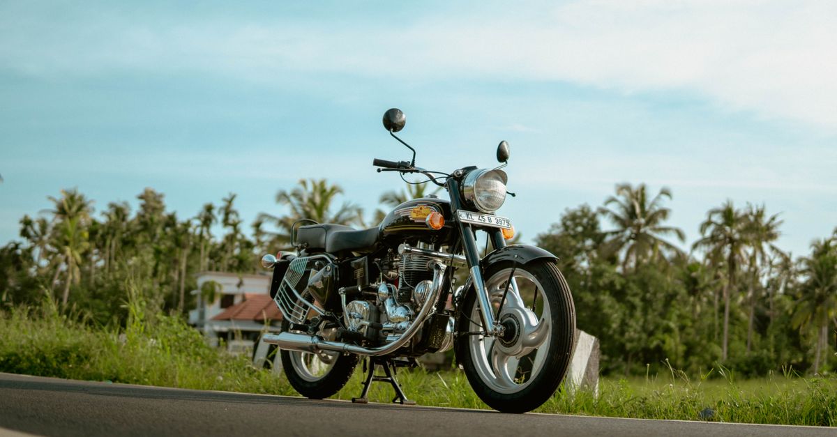 Classic vintage motorcycle parked on a tropical road surrounded by palm trees in Kerala, India.